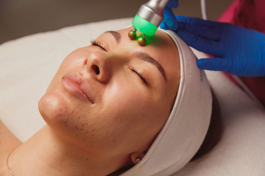 Young woman with acne getting ultrasound skin cleansing and face treatment at beauty salon