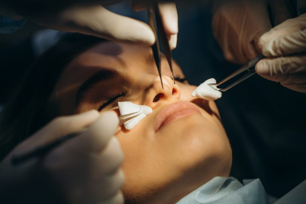 Surgeon and his assistant performing cosmetic surgery on nose in hospital operating room.